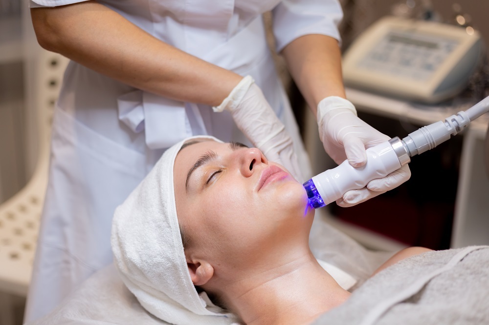 A young beautiful girl lies on the beautician's table and receives procedures with a professional apparatus for skin rejuvenation and moisturizing